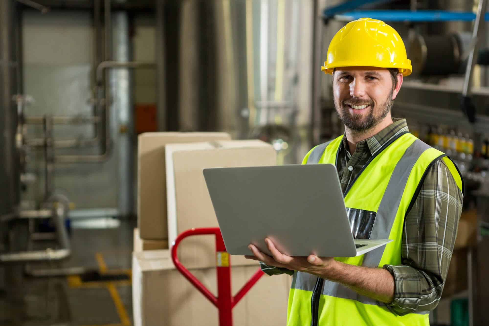 smiling male worker using laptop distribution warehouse 1 - SimbioTecs